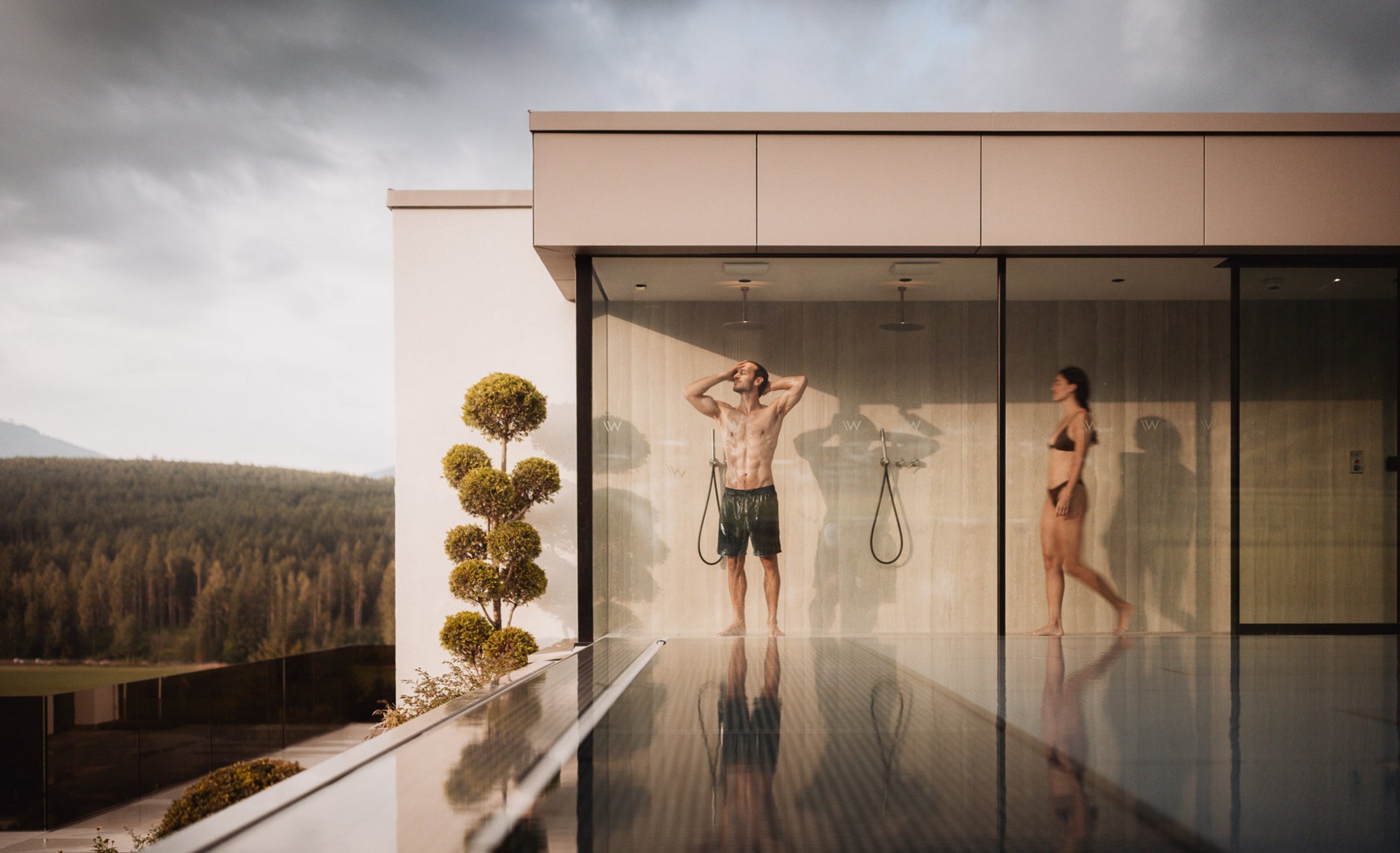 Die Heimat des Strahlens: Ihr Wellnesshotel in Südtirol Personen in Badebekleidung unter Außenduschen eines modernen Gebäudes am Pool