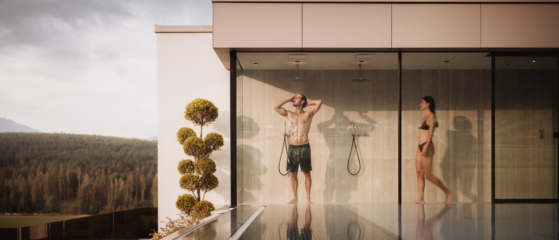 Personen in Badebekleidung unter Außenduschen eines modernen Gebäudes am Pool