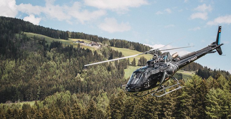 Schwarzer Hubschrauber fliegt über bewaldete Berge und grüne Hügel