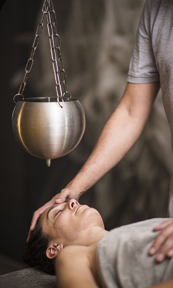 Persona che riceve un massaggio ayurveda alla testa sotto una ciotola di metallo appesa