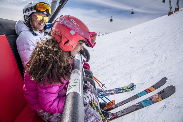 Zwei Skifahrer im Skilift mit Skiern und Helmen bei sonnigem Wetter