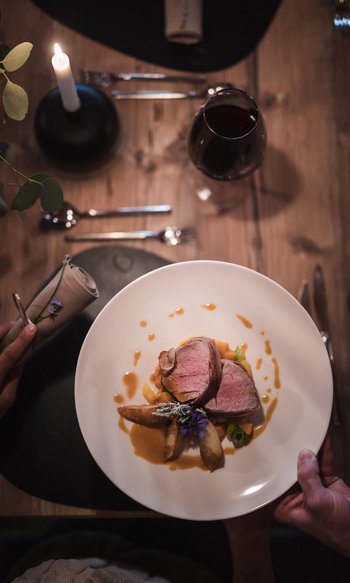 Gedeckter Tisch mit Kerze, Wein und angerichtetem Fleischgericht auf weißem Teller