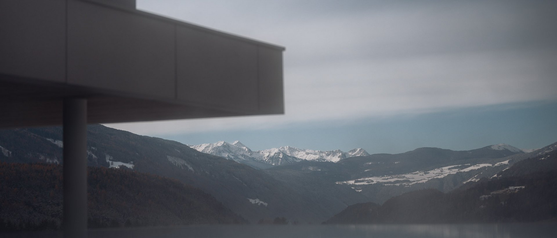 Die Heimat des Strahlens: Ihr Wellnesshotel in Südtirol Moderner Balkon mit Säule vor verschneiten Bergen und ruhigem See im Nebel