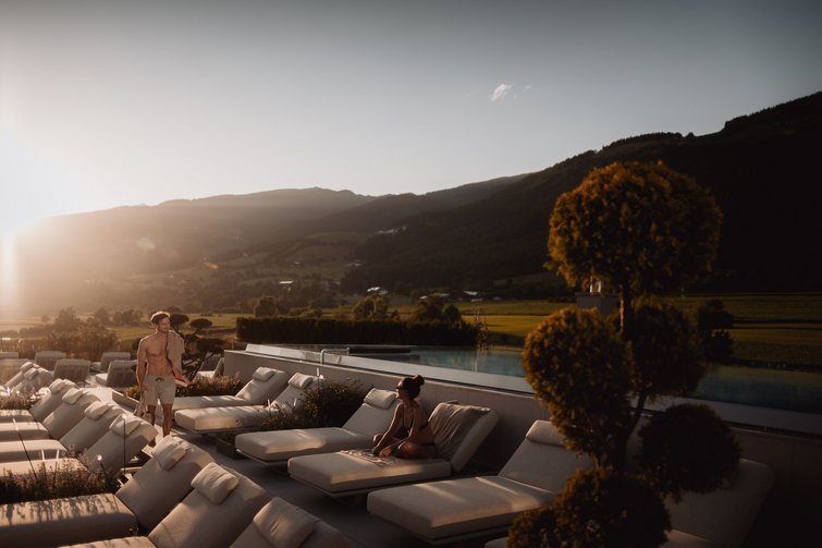 Die Heimat des Strahlens: Ihr Wellnesshotel in Südtirol Menschen entspannen auf Liegestühlen neben Pool in sonniger Berglandschaft