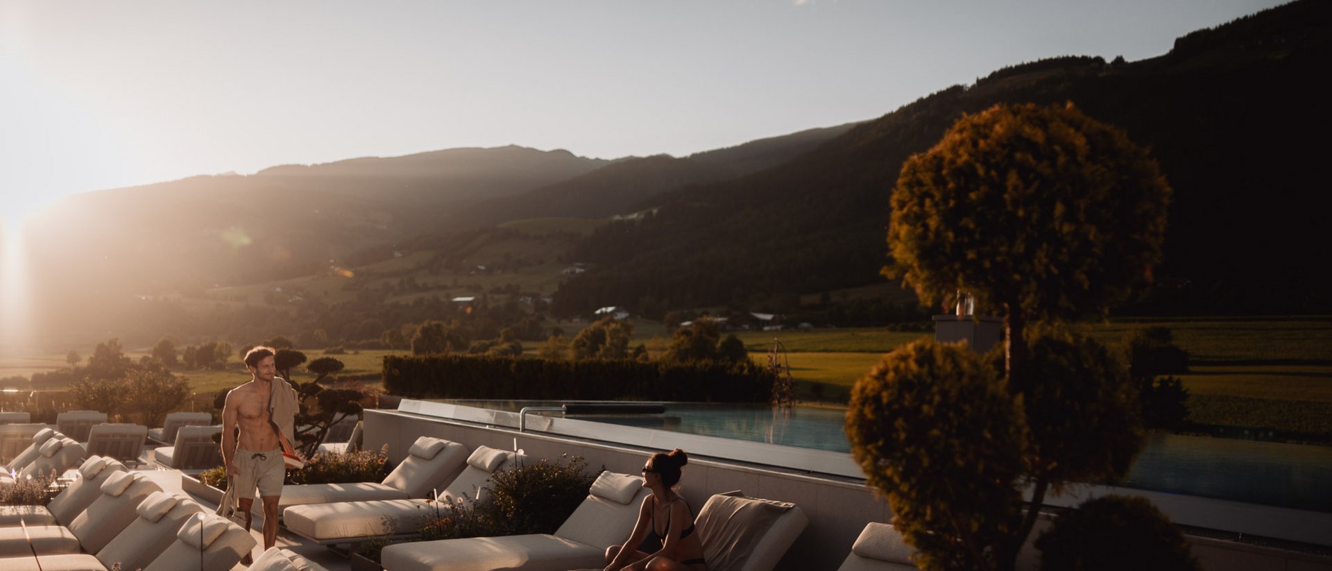 Menschen entspannen auf Liegestühlen neben Pool in sonniger Berglandschaft