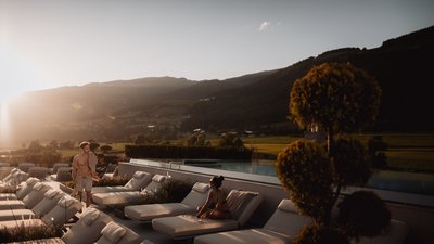 Photos from your hotel in Pfalzen in Val Pusteria/Pustertal People relaxing on lounge chairs by pool in sunny mountain landscape