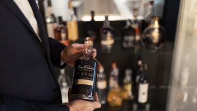 L’esclusività in foto: il nostro chalet in Alto Adige di lusso Persona che tiene una bottiglia di rum Dos Maderas davanti a uno scaffale di liquori