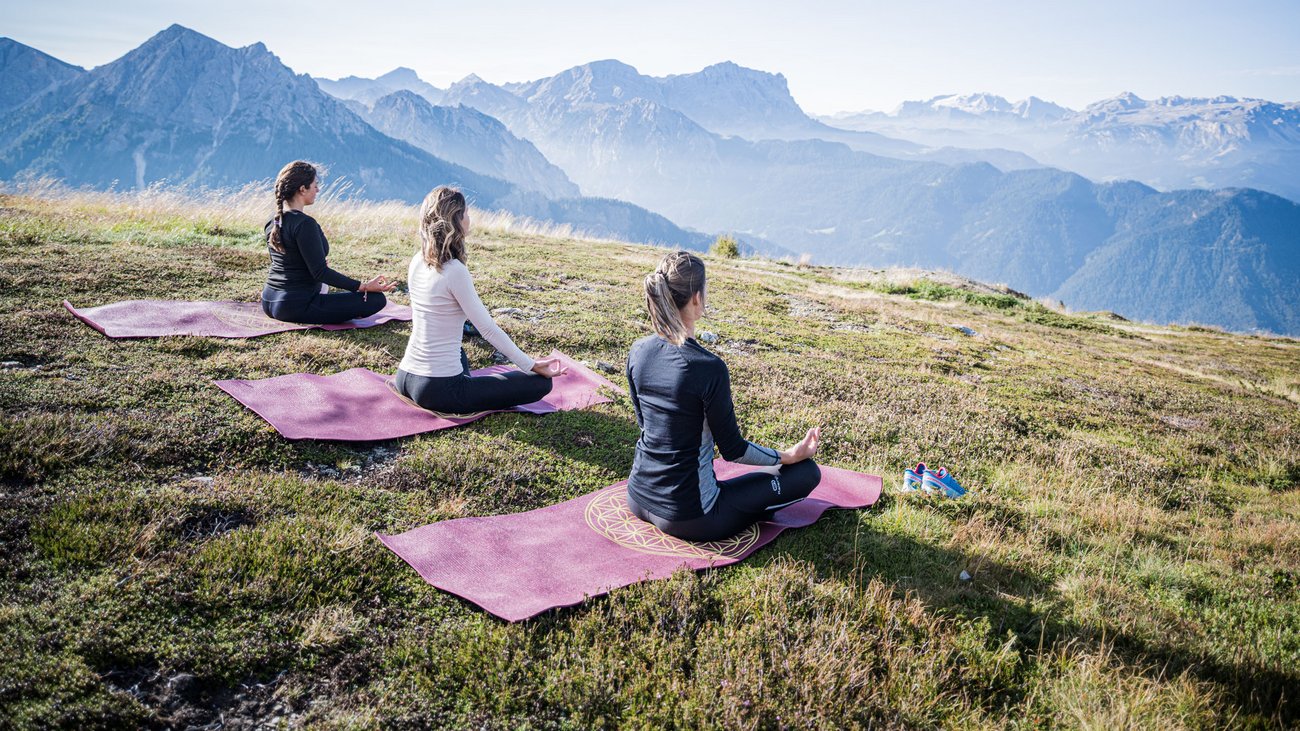 Tre donne fanno meditazione su tappetini da yoga in montagna con cielo limpido