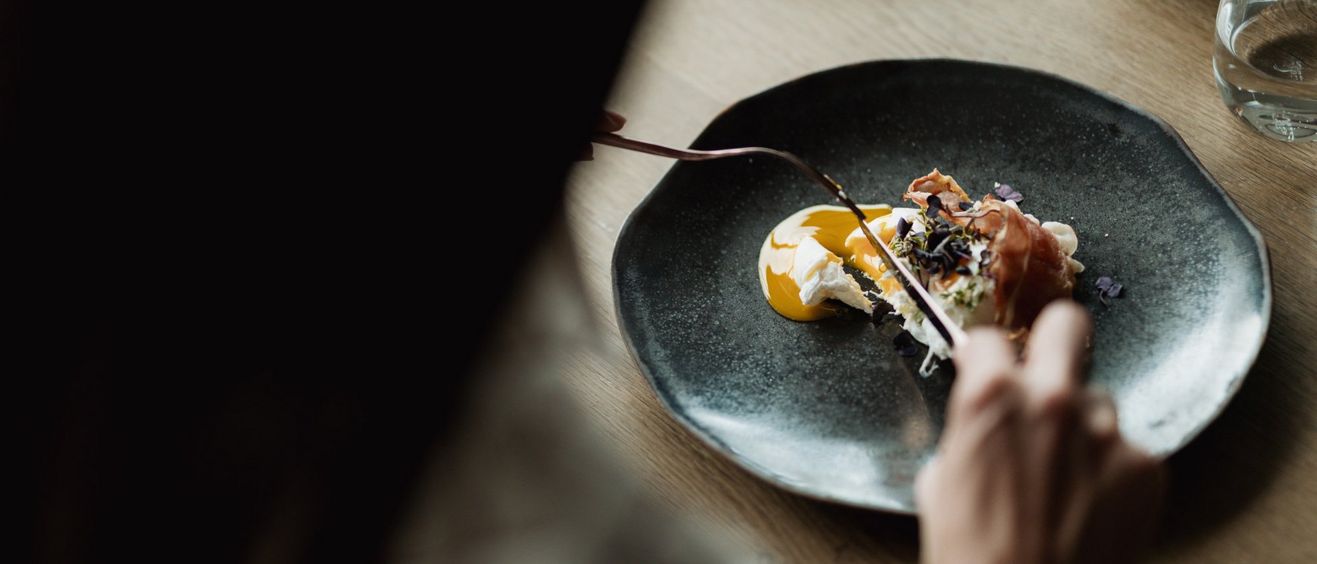 Person isst Gericht mit Ei und Schinken auf schwarzem Teller