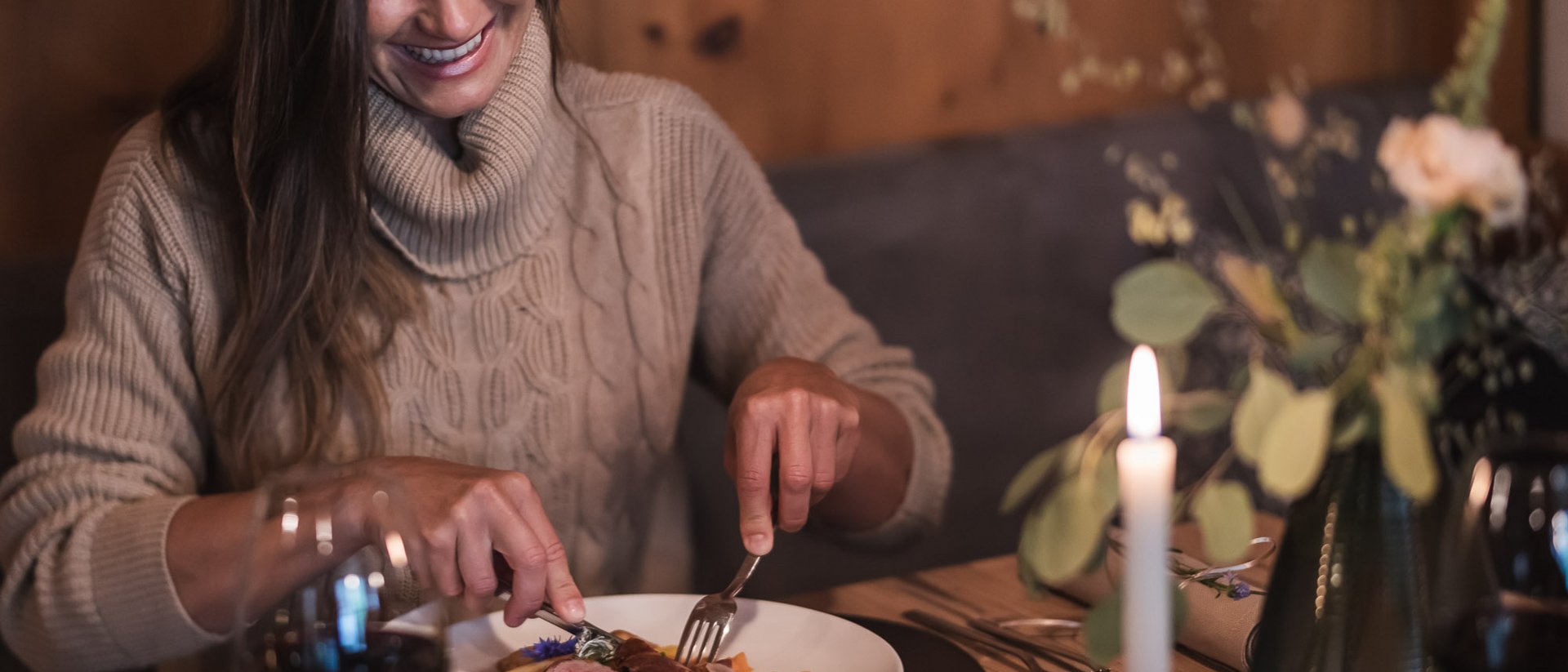 Il benessere nasce qui: il nostro hotel in Val Pusteria Donna con maglione beige che mangia un piatto in un ristorante accogliente