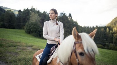 Donna a cavallo di un cavallo marrone in un paesaggio verde con montagne