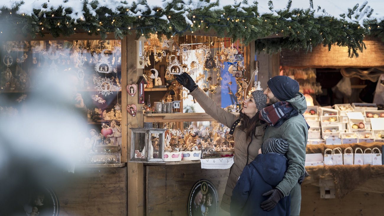 Familie schaut sich handgefertigten Weihnachtsschmuck auf Marktstand an