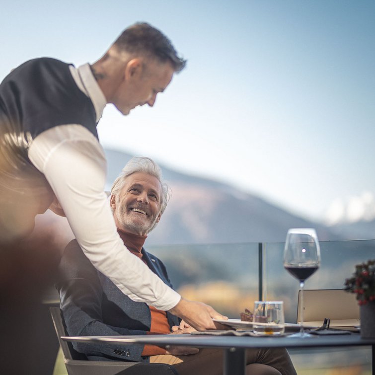 Cameriere serve uomo anziano in terrazza con vista montagna