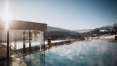 Anreise in Ihr Wellness-, Aktiv- und Skihotel im Pustertal Dampfender Außenpool mit Bergblick bei klarem Himmel und Sonnenlicht