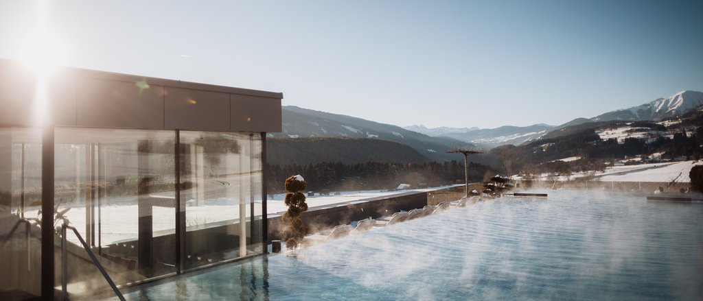 Der facettenreiche Spa unseres Spa-Hotels in Südtirol Dampfender Außenpool mit Bergblick bei klarem Himmel und Sonnenlicht