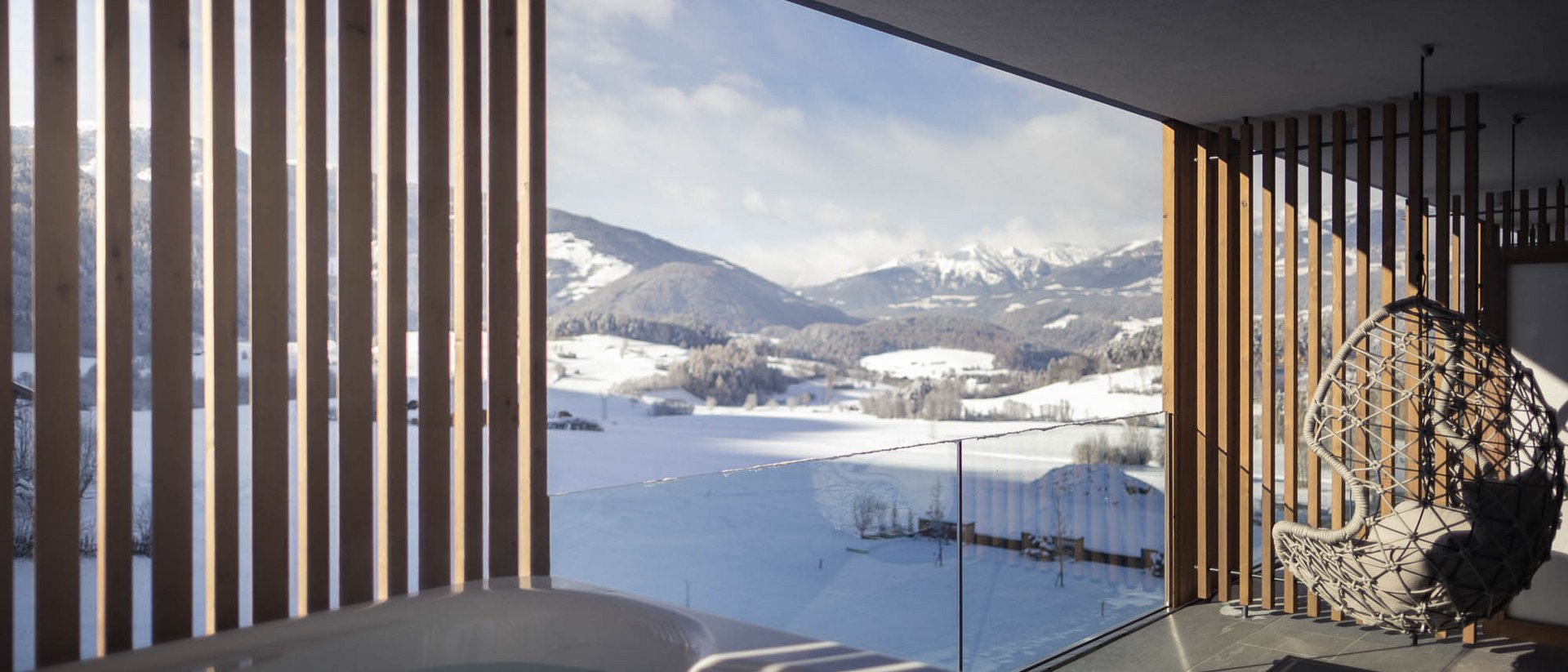 Balcone con vasca idromassaggio e sedia sospesa con vista sulle montagne innevate