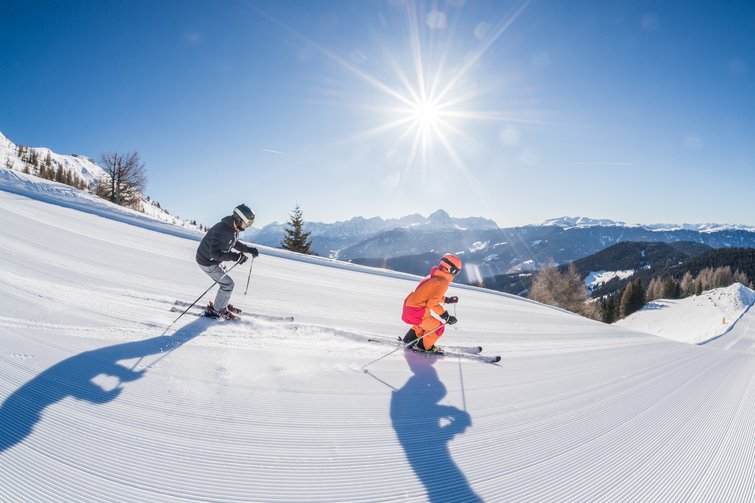 Zwei Skifahrer bei sonnigem Wetter auf präparierter Piste in den Bergen