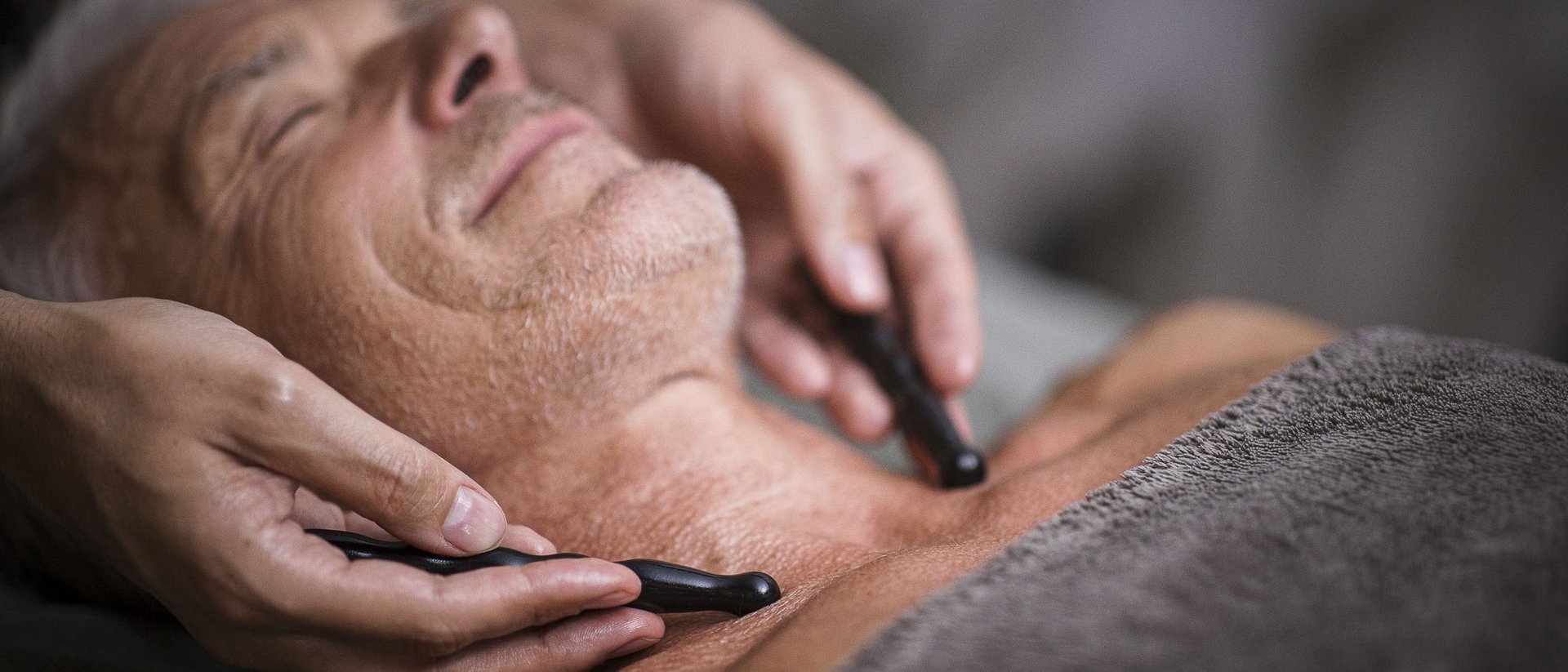 Mann erhält Gesichtsmassage mit Massagestäben auf Brust und Nacken