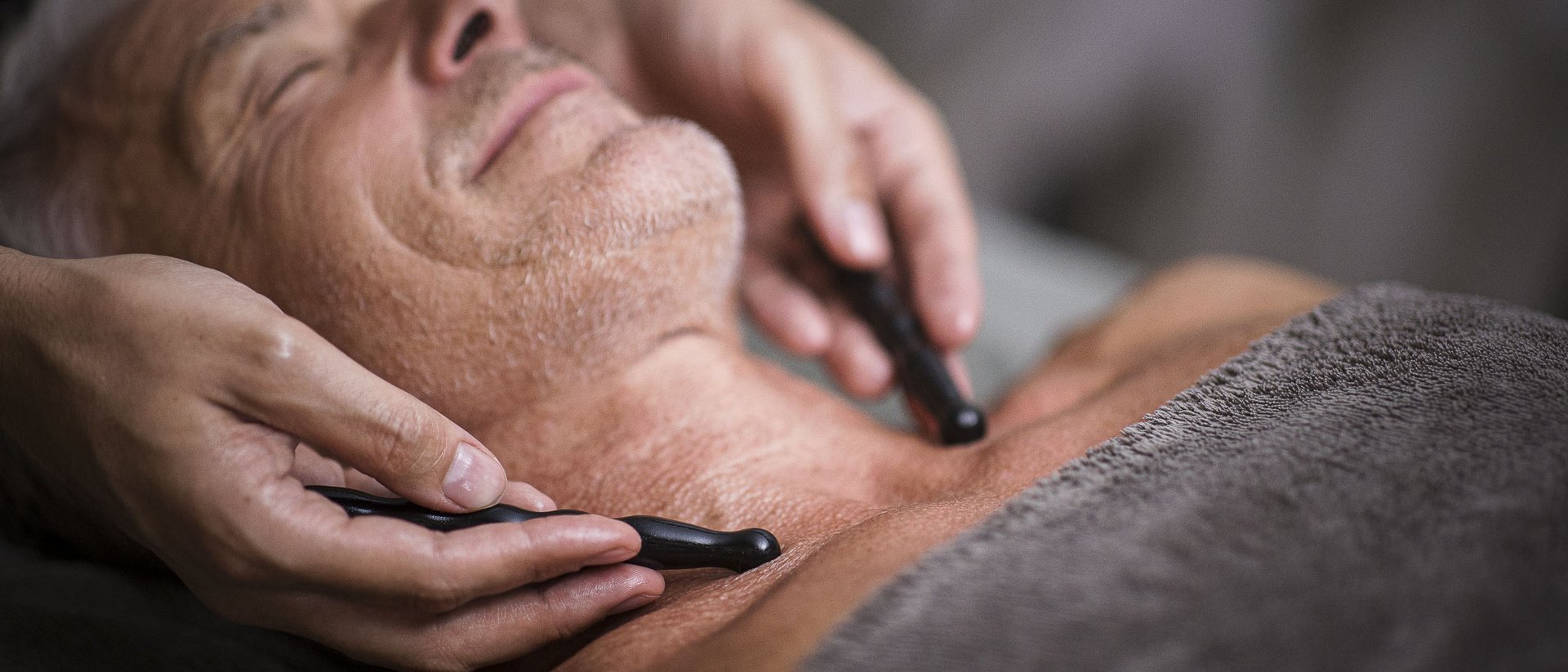 Mann erhält Gesichtsmassage mit Massagestäben auf Brust und Nacken