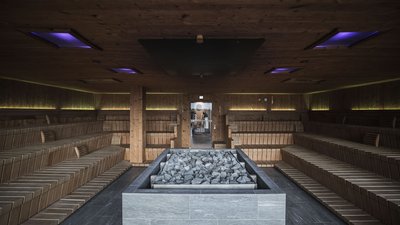 Ampia sauna in legno con forno di pietra al centro e file di sedute ai lati