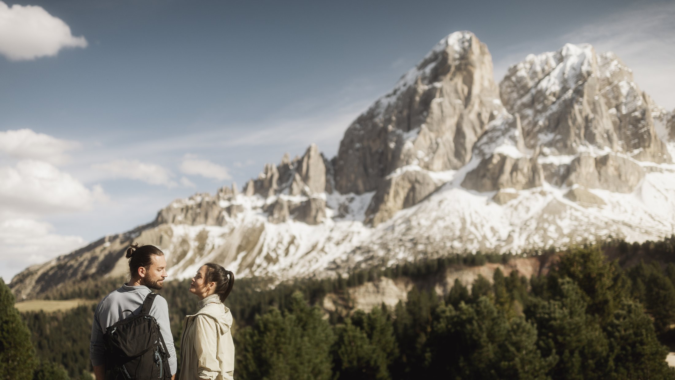 Coppia che cammina davanti a montagne innevate e foreste verdi con cielo sereno