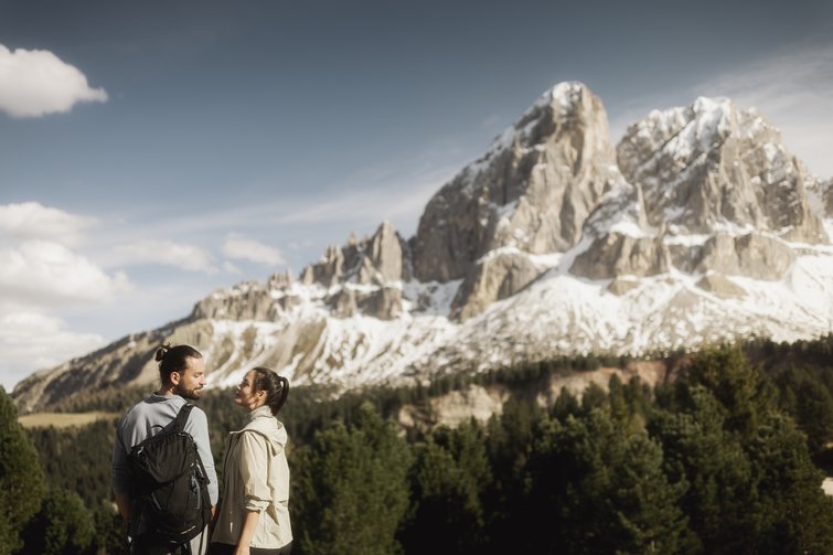 Coppia che cammina davanti a montagne innevate e foreste verdi con cielo sereno