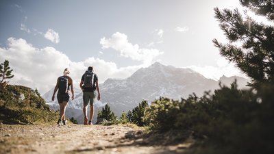 Due escursionisti su un sentiero di montagna con montagne innevate sullo sfondo