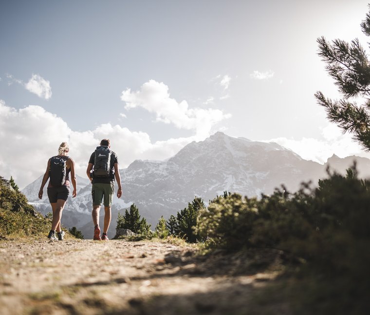 Due escursionisti su un sentiero di montagna con montagne innevate sullo sfondo