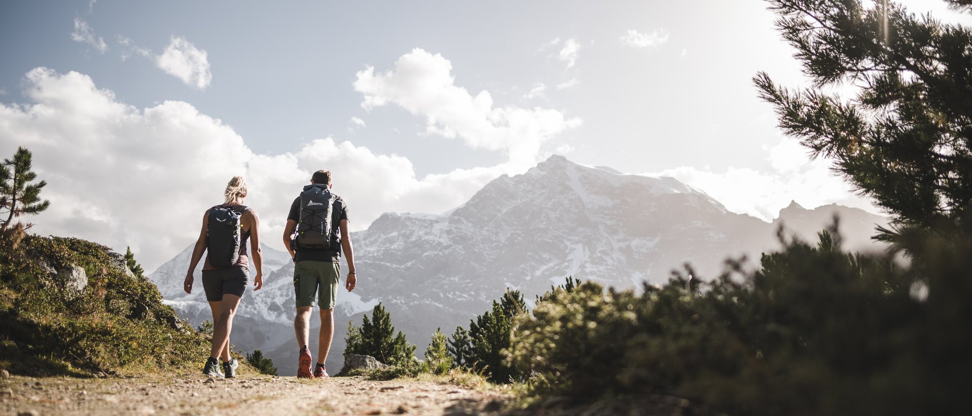 Due escursionisti su un sentiero di montagna con montagne innevate sullo sfondo