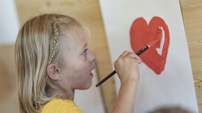 Bambina dipinge un cuore rosso su un foglio con un pennello