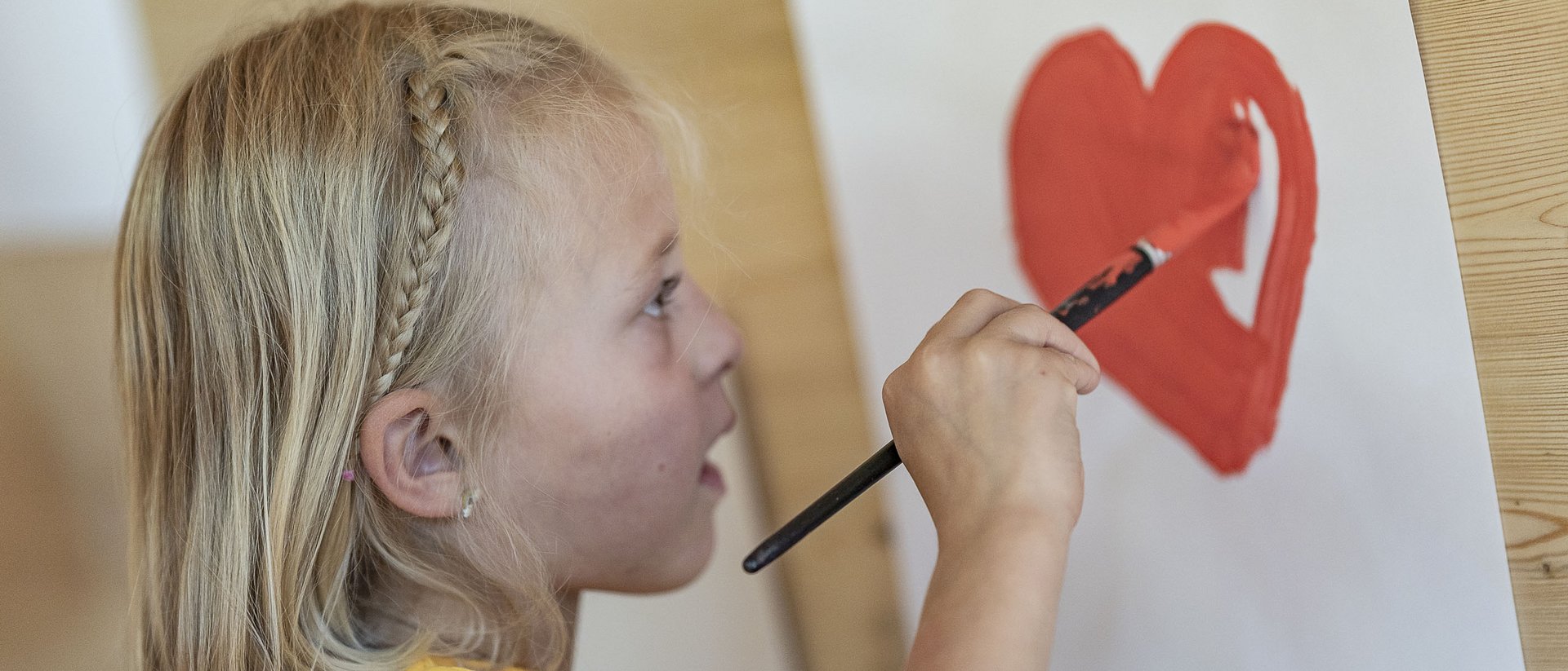 Child painting a red heart on paper with a brush