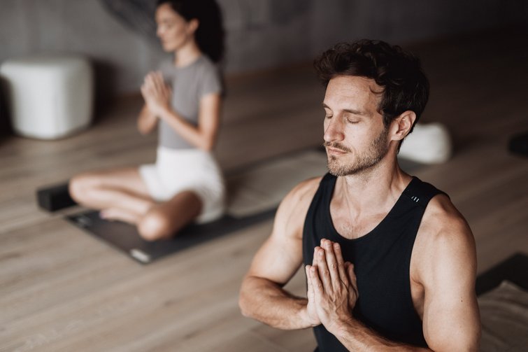 Uomo e donna meditano insieme con occhi chiusi e mani giunte