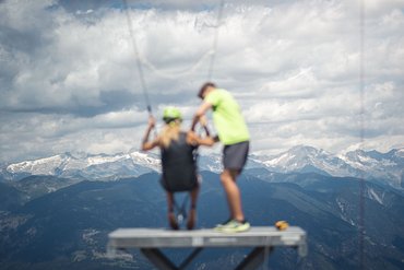 Two people with mountain backdrop, one sitting on a swing