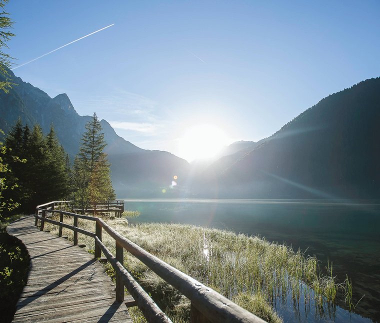Sentiero in legno sul lago con alba e montagne sullo sfondo