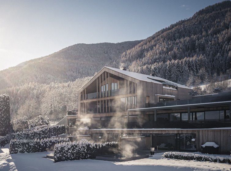 Modern wooden house with snow and mist in front of forested mountain
