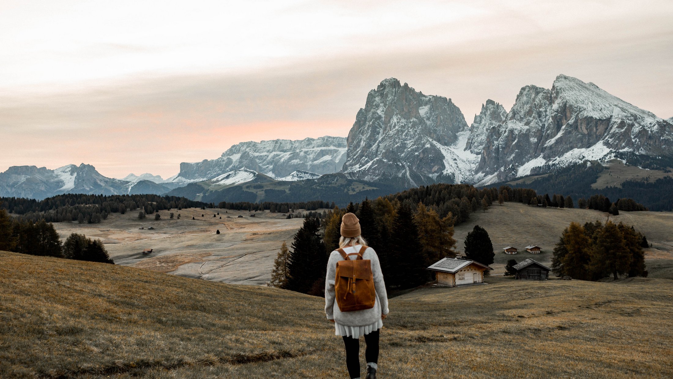 Donna con zaino cammina in un prato di montagna con le Alpi sullo sfondo