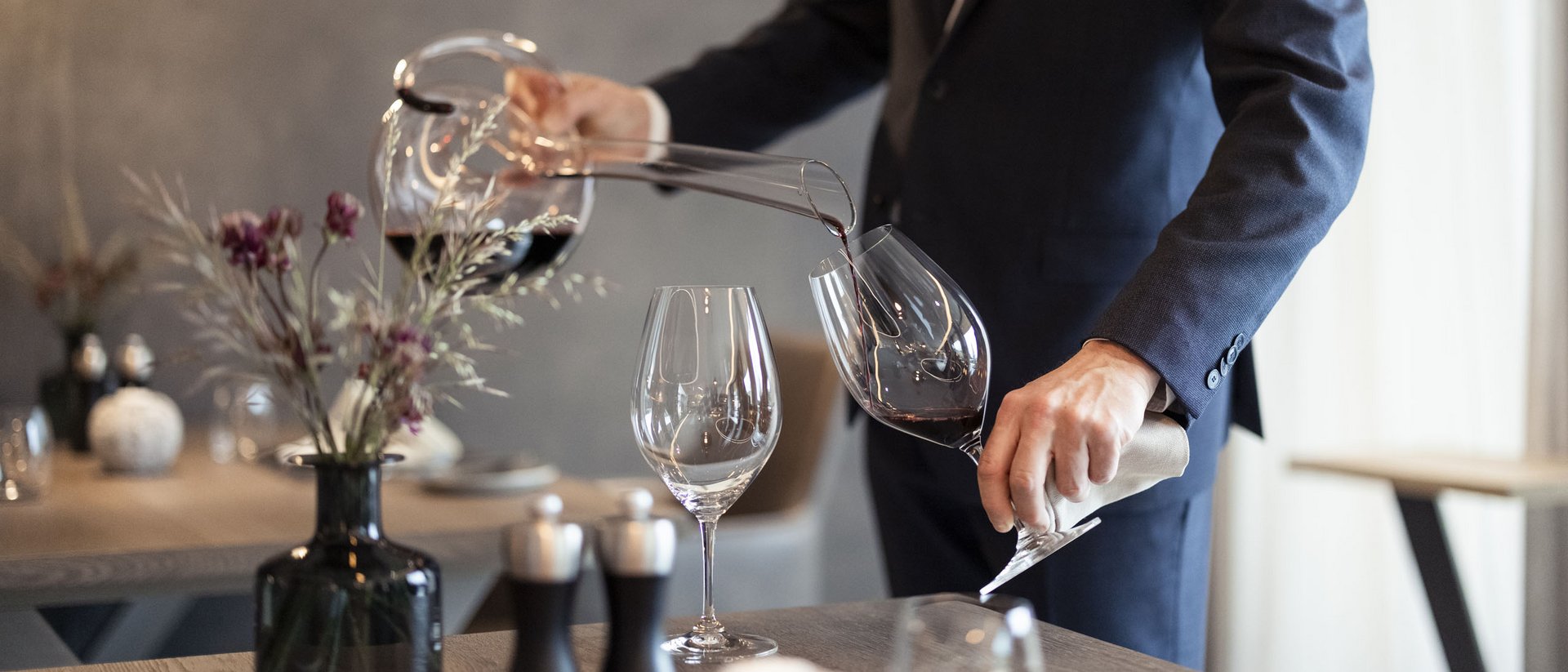 Mann in Anzug schenkt Rotwein aus Dekanter in Glas ein