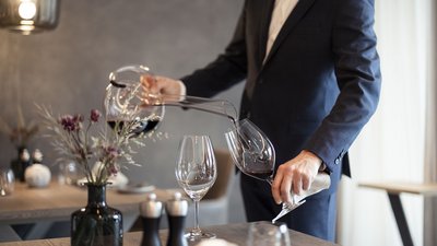 Uomo in abito versa vino rosso da decanter in bicchiere