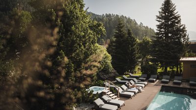 The best photos from our hotel in South Tyrol that kids love Woman relaxing on lounge chair by pool surrounded by trees and mountains