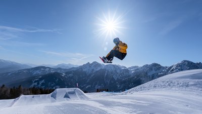 Snowboarder springt bei sonnigem Wetter vor Bergkulisse