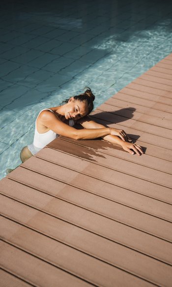 Donna rilassata appoggiata al bordo di una piscina con costume bianco