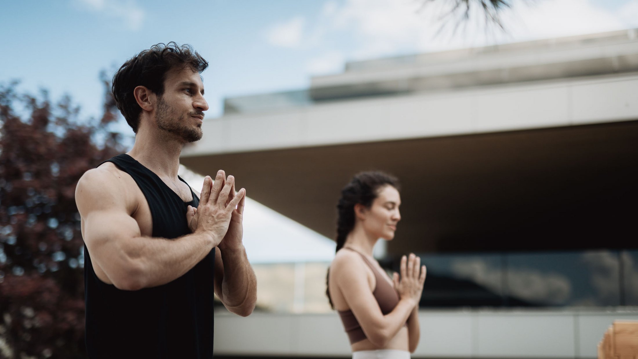 Uomo e donna praticano yoga all'aperto con mani unite