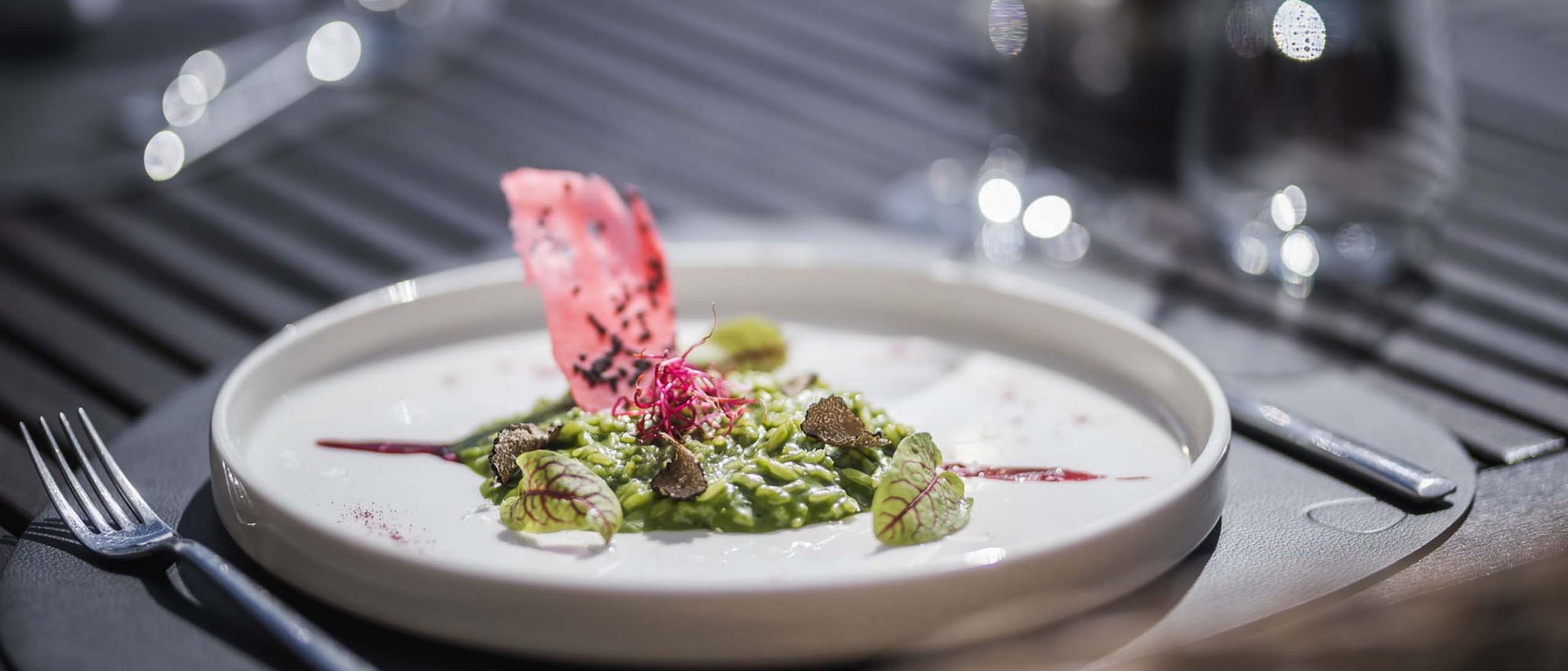 Kreatives grünes Risotto auf weißem Teller mit roten und grünen Garnituren