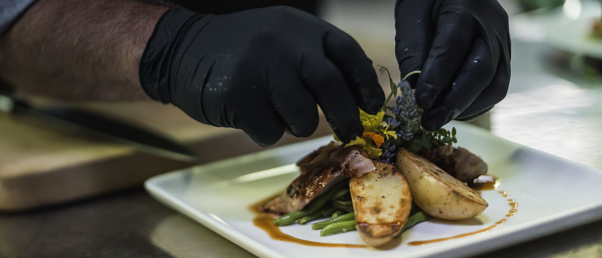 Koch mit schwarzen Handschuhen dekoriert fein angerichtetes Gericht auf weißem Teller