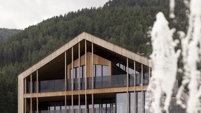 L’esclusività in foto: il nostro chalet in Alto Adige di lusso Casa moderna in legno davanti a montagna boscosa con fontane d'acqua in primo piano