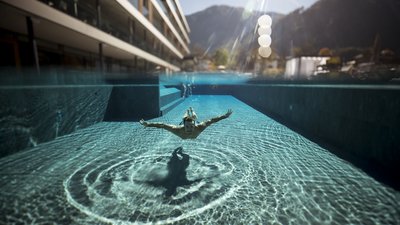 Persona nuota sott'acqua in piscina limpida con sole e montagne sullo sfondo