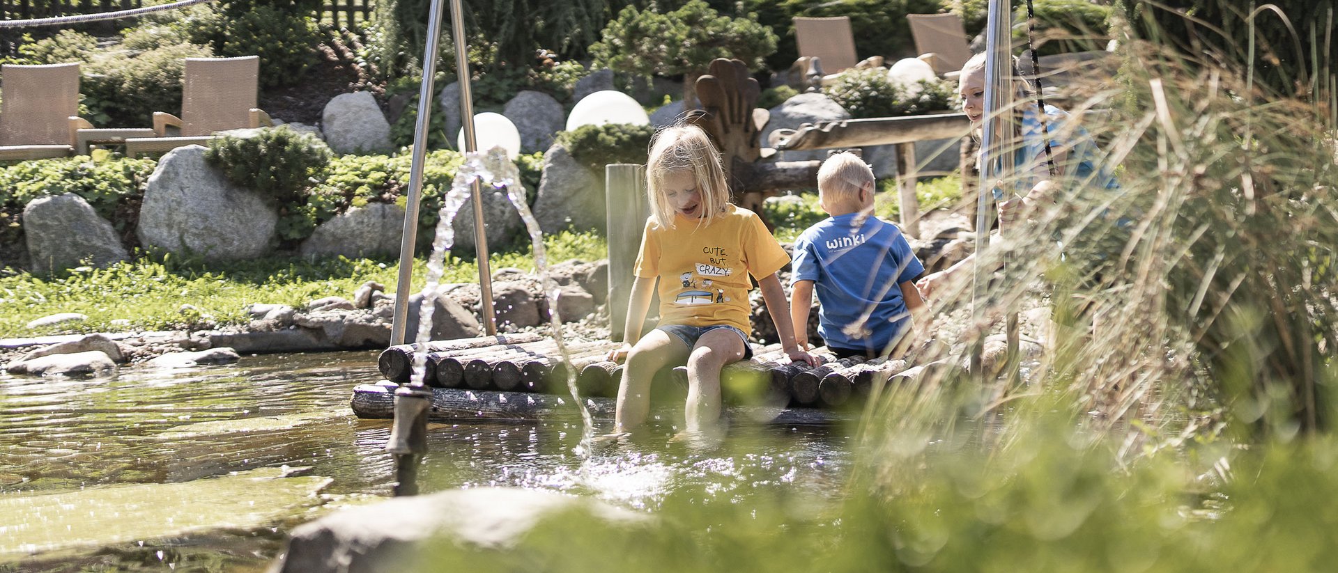 Children sitting on a wooden raft playing by a sunny pond