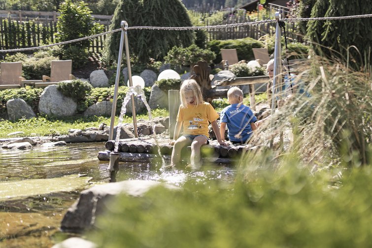 Kinder sitzen auf einem Holzfloß und spielen am sonnigen Teich