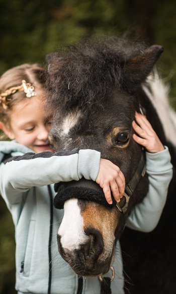 Bambina abbraccia e accarezza un pony nero con macchia bianca