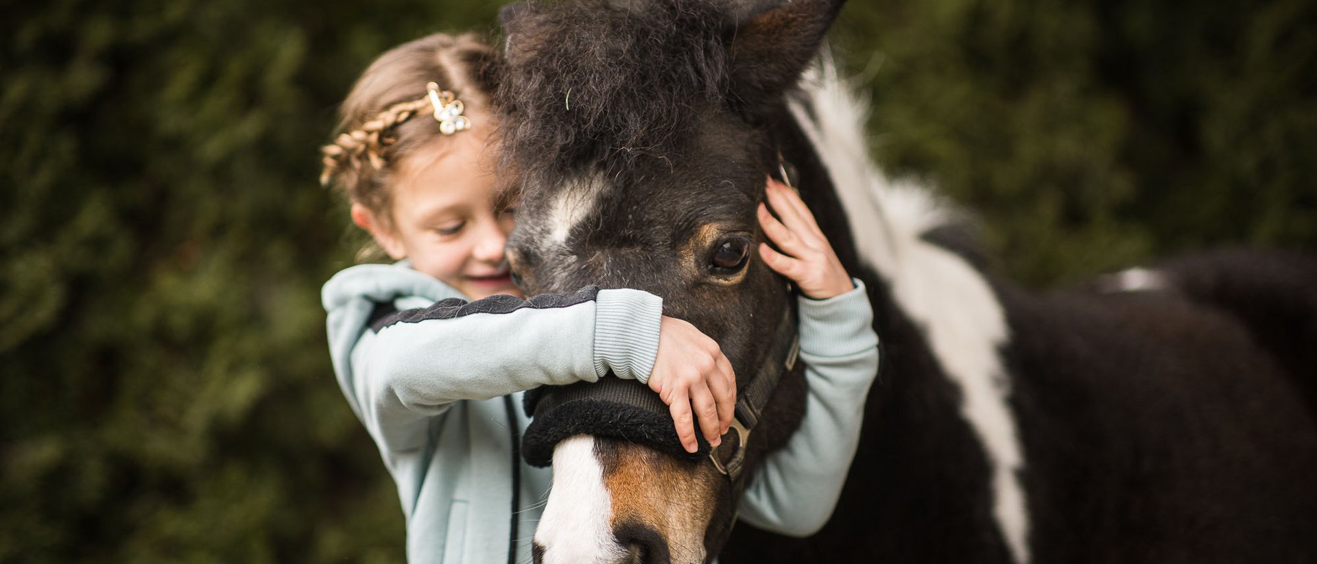 Dove fare equitazione in Alto Adige: hotel con maneggio Bambina abbraccia e accarezza un pony nero con macchia bianca